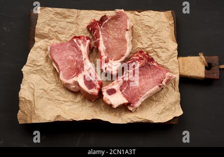 trois tranches de porc juteuses crues sur la côte, la nourriture repose sur du papier parchemin brun Banque D'Images