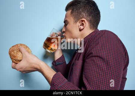 homme gai ivre avec une tasse de bière et un hamburger à la main régime alimentaire style de vie fond bleu Banque D'Images