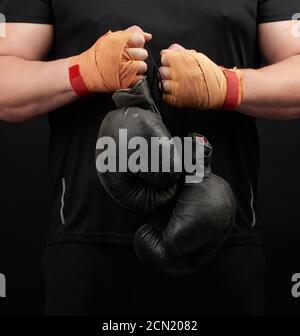 athlète musculaire en uniforme noir tient très vieux gants de boxe noirs dans sa main, ses mains sont ba Banque D'Images