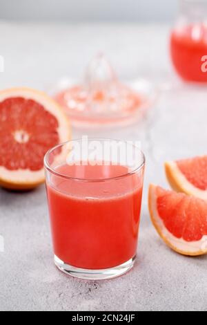 Un verre de jus de pamplemousse fraîchement préparé et des tranches de fruits frais sur fond de béton léger. H Banque D'Images