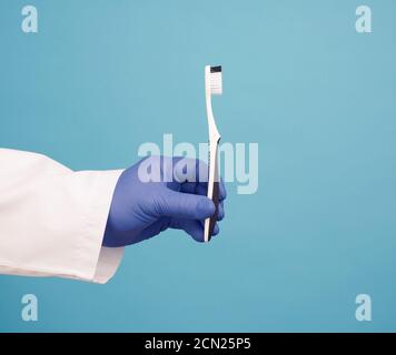 médecin en robe blanche uniforme et gants bleus stériles tenir une brosse à dents Banque D'Images