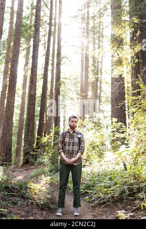 Adolescent debout dans redwood grove avec masque pendant COVID-19 Banque D'Images