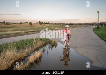 des vélos de jeune fille ludiques à travers une flaque d'eau dans un parc Banque D'Images