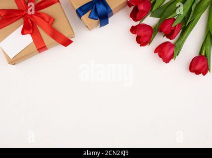 bouquet de tulipes rouges fleuris avec des feuilles vertes, cadeau emballé dans du papier brun sur un dos blanc Banque D'Images
