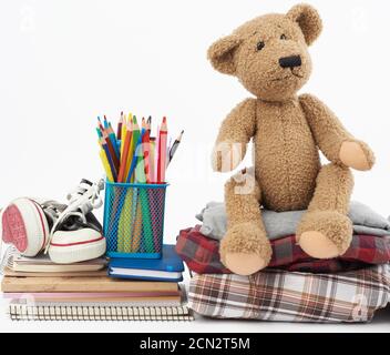 pile de vêtements pliés, de baskets de sport, de papeterie et d'ours en peluche marron sur fond blanc Banque D'Images