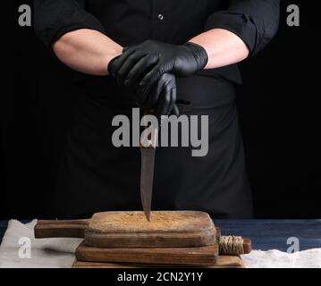 chef dans une chemise noire et gants en latex noir tient un couteau de cuisine vintage pour couper de la viande Banque D'Images