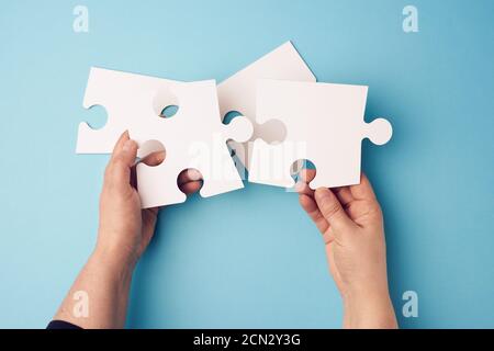 deux mains de femme tenant de gros papier blanc puzzles sur un arrière-plan bleu Banque D'Images