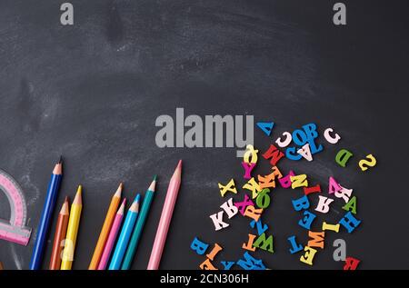 crayons en bois multicolores, lettres sur un panneau en bois noir, concept d'apprentissage Banque D'Images