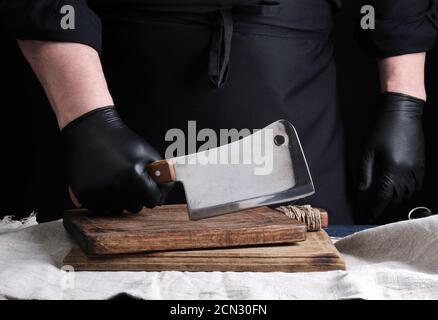 porte-gants de cuisine en uniforme noir et en latex noir pour hommes un grand couteau à viande tranchant sur un sanglier Banque D'Images