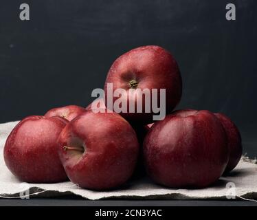 un bouquet de pommes mûres rouges repose sur une serviette en lin grise, sur fond noir Banque D'Images