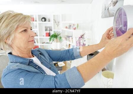 femme mûre accrochant l'horloge sur le mur Banque D'Images