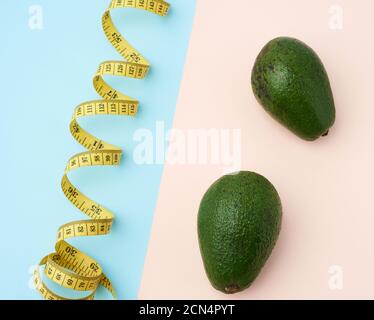 deux fruits vert avocat et un ruban de mesure torsadé jaune sur fond beige-bleu Banque D'Images