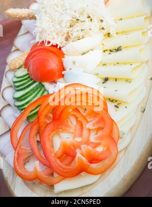 Trancheuse simple d'en-cas variés : poivron rouge, fromage, jambon sur une assiette en bois Banque D'Images