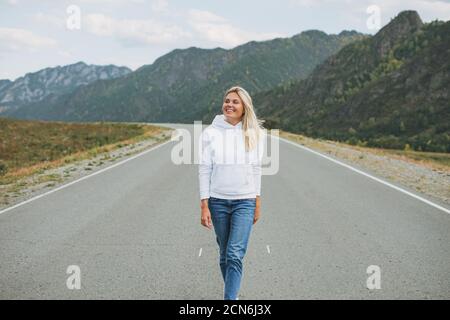 Belle blonde souriante jeune femme voyageur dans blanc à capuche sur la route, voyage à la montagne, Altai Banque D'Images