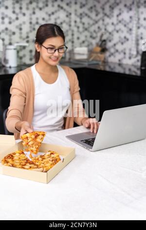Femme asiatique travaille à la maison dans la cuisine et manger livraison de pizza emporter la nourriture et prendre le café pendant ville de verrouillage de Banque D'Images