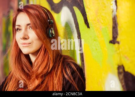portrait d'une jeune femme à tête rouge avec casque sur un mur de graffiti coloré Banque D'Images
