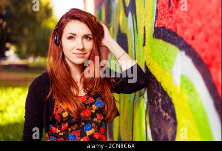 portrait d'une jeune femme à tête rouge avec casque sur un mur de graffiti coloré Banque D'Images