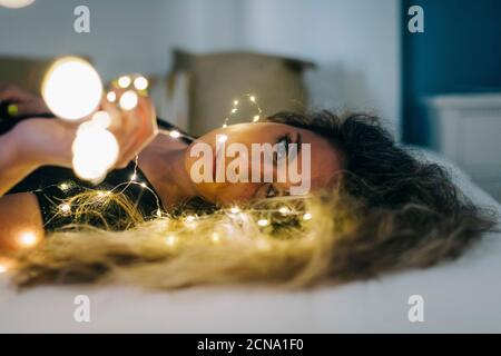 Portrait sereine jeune femme avec des guirlandes de lumières sur le lit Banque D'Images