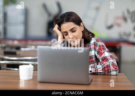 Portrait d'une femme indienne fatiguée travaillant sur son ordinateur portable, assise dans une cafétéria de bureau, café-restaurant, environnement de travail décontracté, humeur endormi, yeux fermés Banque D'Images