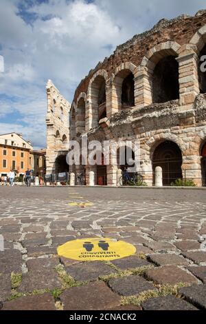 Marqueur de distance Covid jaune sur la route à l'extérieur de l'Arena di Verona sur la Piazza Bra, Vérone, Vénétie, Italie, Europe. Banque D'Images