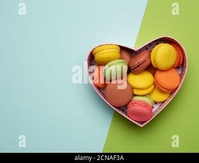 des macarons multicolores cuits ronds sont disposés dans une boîte en carton rouge en forme de coeur Banque D'Images