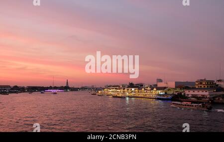 Bangkok, Thaïlande, 26 décembre 2018. Éclairage lumineux des restaurants sur les rives de la rivière Chao Phraya au coucher du soleil. Nuages roses sur la veille Banque D'Images