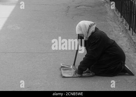 Chernihiv, Ukraine, 7 juin 2019. Une femme âgée dans un foulard supplie pour de l'argent, s'agenouillant dans une rue de ville. Monochrome. Banque D'Images