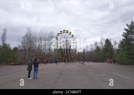 Pripyat, Ukraine, 14 mars 2020. Touristes près de la célèbre grande roue dans un parc d'attractions abandonné à Pripyat. Temps nuageux, le ciel est couvert Banque D'Images