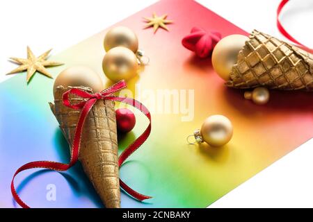 Décorations de Noël en couleurs de drapeau arc-en-ciel de la communauté LGBTQ. Cornet de gaufres à la crème glacée, étoiles de boules dorées et forme de coeur sur papier arc-en-ciel, LGBT Banque D'Images