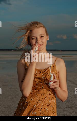 Femme souriante avec un spray respiratoire et un spray pour la gorge dans ses mains sur le rivage d'un lac salé, portrait d'une femme souffrant des voies respiratoires Banque D'Images