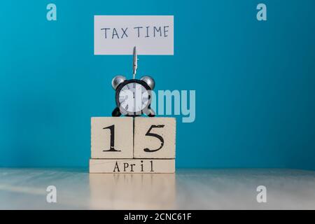 Concept de rappel de jour d'imposition. 15 avril calendrier en bois et réveil avec bannière et phrase manuscrite 'tax time' sur table en bois. Banque D'Images