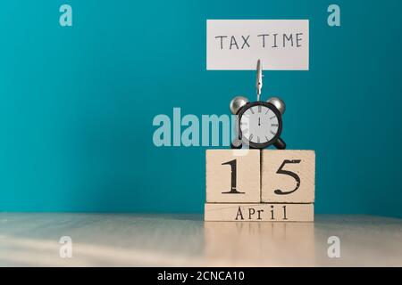 Concept de rappel de jour d'imposition. 15 avril calendrier en bois et réveil avec bannière et phrase manuscrite 'tax time' sur table en bois. Banque D'Images