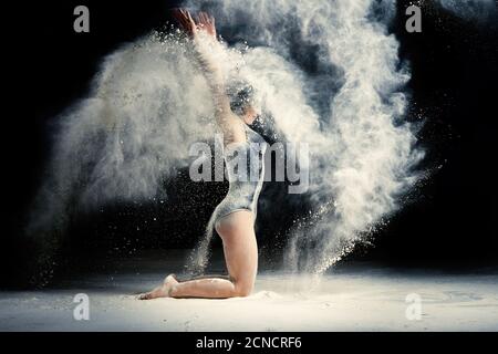 Femme caucasienne avec un corps athlétique assis sur le sol et jette la farine blanche vers le haut, Banque D'Images