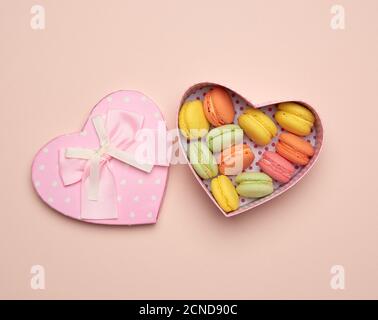 les macarons multicolores cuits ronds sont dans une boîte en carton rose en forme de coeur Banque D'Images