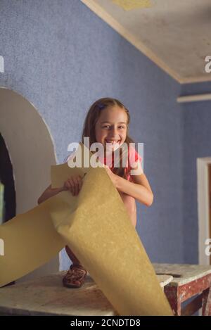 fille retirer les vieux papiers peints du mur. Fille aide à coller le papier peint. Un adolescent aide ses parents. Accueil Banque D'Images