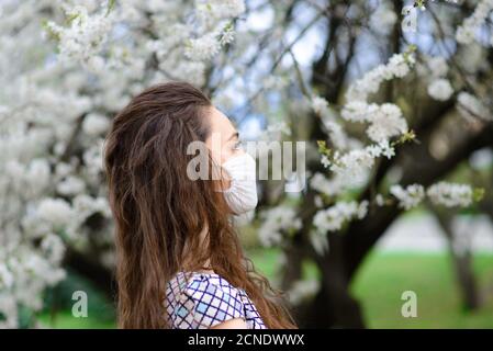 Fille, jeune femme dans un masque médical stérile de protection sur son visage dans le jardin de printemps. Pollution, virus, coronavirus pandémique concept.