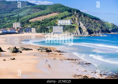 Vue sur la plage de la ville de Bakio. Les gens marchent sur le sable à marée basse. Près de Bilbao et Gaztelugatxe, pays basque, Nord de l'Espagne. Banque D'Images