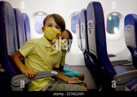 Tout-petit garçon, enfant arnaquant dans l'avion, assis et attendant le départ, jouant avec des jouets, souriant heureux Banque D'Images