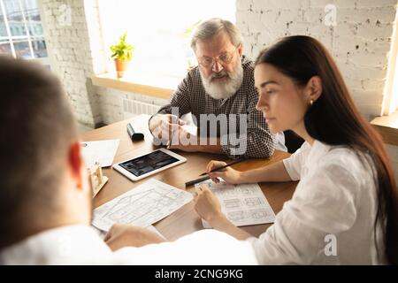 Un architecte-ingénieur de sexe masculin présente un projet de future maison pour la jeune famille. Homme travaillant au bureau avec des documents, un plan. Première maison, industriel, concept de bâtiment. Déplacement vers un nouveau lieu de vie. Banque D'Images