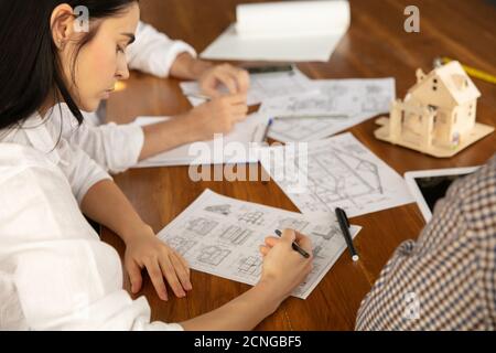 Jeune famille à l'écoute de l'architecte-ingénieur mâle présente le projet . Travailler au bureau avec des documents, un plan. Première maison, industriel, concept de bâtiment. Déplacement vers un nouveau lieu de vie. Banque D'Images