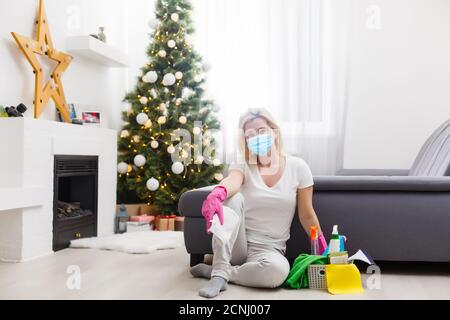 Belle jeune femme fait le nettoyage de la maison. La fille frotte la poussière. Femme en gants et masque de protection est d'essuyer la poussière à l'aide d'un spray et d'un plumeau tout en Banque D'Images