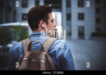 Portrait de jeune gai beau et beau homme bien habillé avec des écouteurs pensant au nouveau projet. Banque D'Images