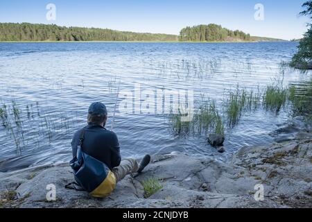 Homme de repos avec un sac scellé se trouve au bord du lac sur la côte rocheuse et apprécie le paysage magnifique. Style de vie. Banque D'Images