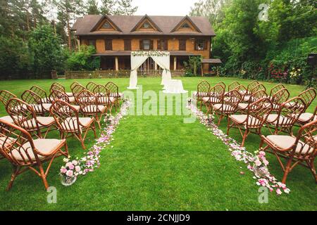 Décoration de cérémonie de mariage extérieure. Chemin avec pétales, chaises décorées de rubans colorés, arc blanc. Banque D'Images