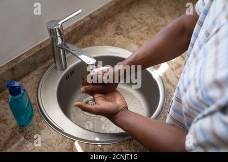 Homme senior afro-américain debout dans une salle de bain, se lavant les mains, distanciation sociale et auto-isolement en quarantaine Banque D'Images