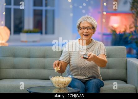 Femme âgée regardant un projecteur, une télévision, des films avec pop-corn le soir. Le retraité passe du temps à la maison. Banque D'Images