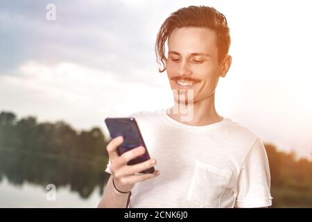 Jeune homme marchant près de la magnifique baie en utilisant le téléphone pour communiquer avec des amis Banque D'Images