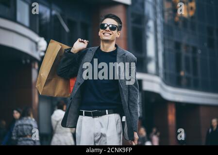 Jeune homme sérieux et élégant avec des lunettes de soleil marchant dans la rue urbaine Et profiter des magasins du Vendredi fou dans les magasins branchés de la ville Banque D'Images