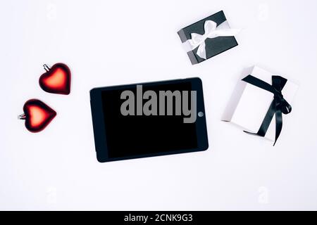 Boîtes-cadeaux noires et blanches, boules en forme de coeur de l'arbre de Christmass et comprimé électonique sur fond blanc. Composition de pose pour anniversaire, Noël, mariage. Concept d'achat en ligne. Banque D'Images