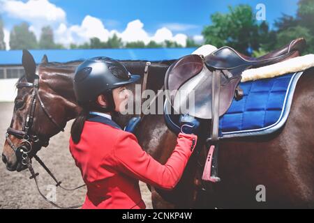 Fille Rider règle la selle sur son cheval pour prendre part aux courses de chevaux. Banque D'Images